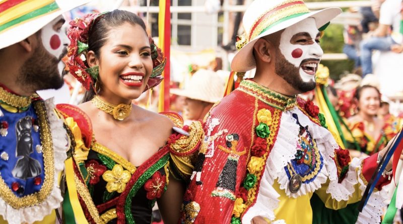 cultural picture showing two men and a woman dressed in brightly colored clothes and makeup smiling