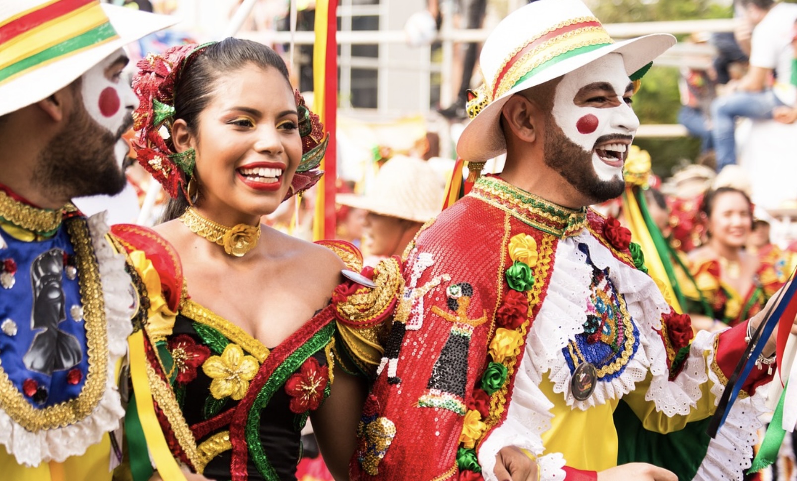 cultural picture showing two men and a woman dressed in brightly colored clothes and makeup smiling