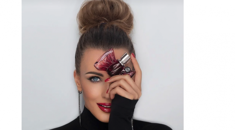 woman holding perfume bottle against her head smiling