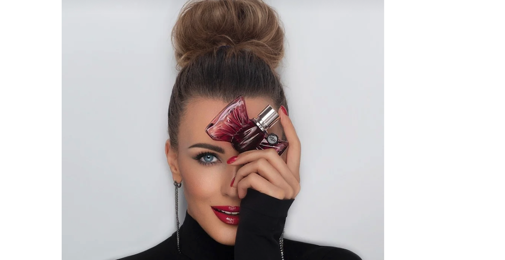 woman holding perfume bottle against her head smiling