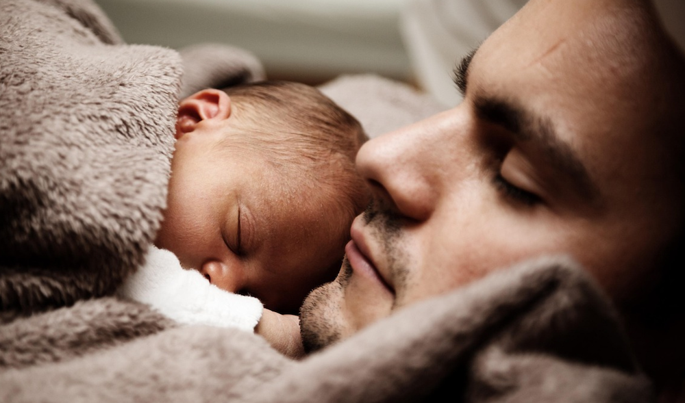 father holding baby in blanket tightly, while wrapped in blankets.