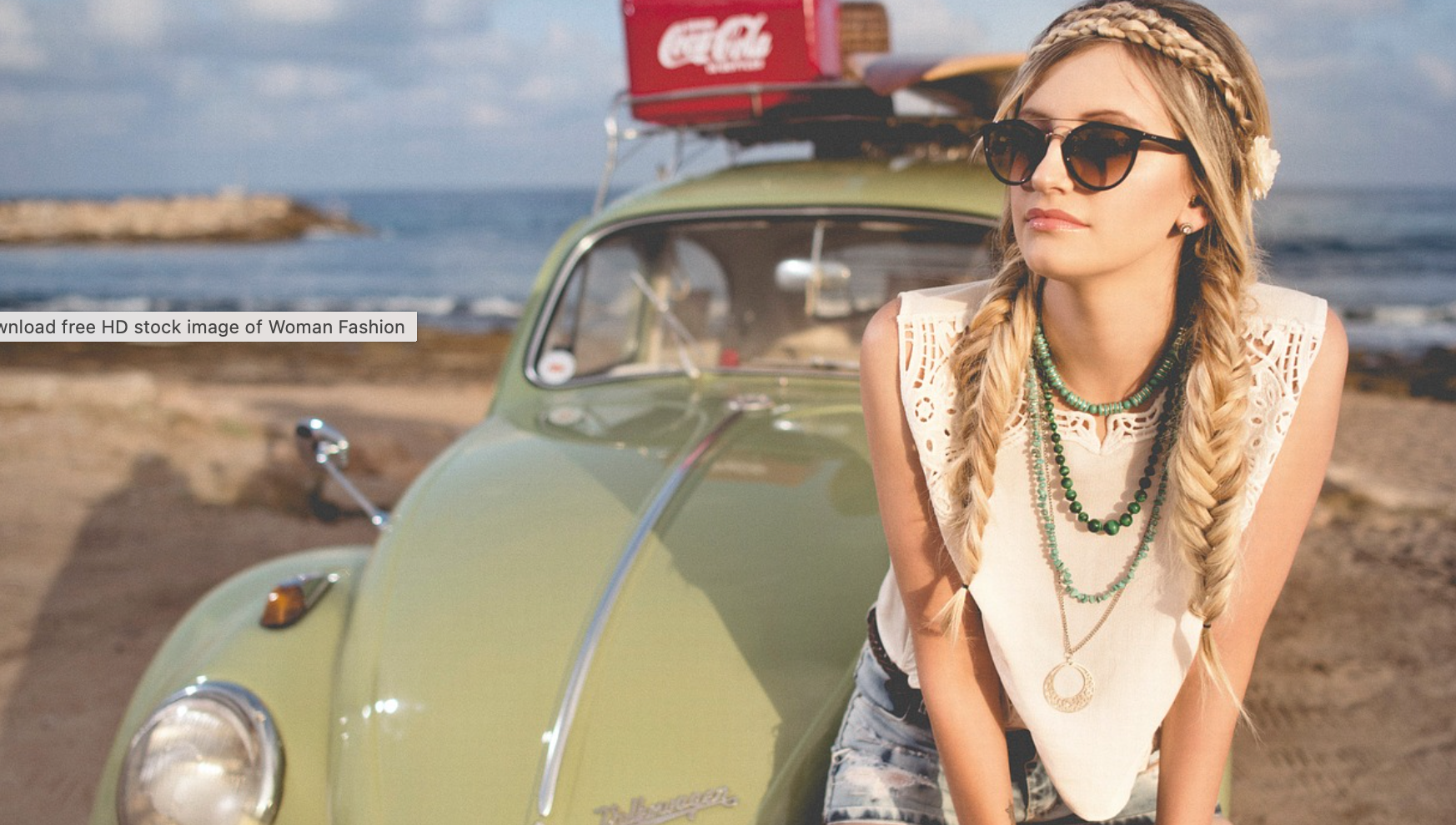 blonde girl sitting on green vw bug with braided hair and dark sunglasses on a beach