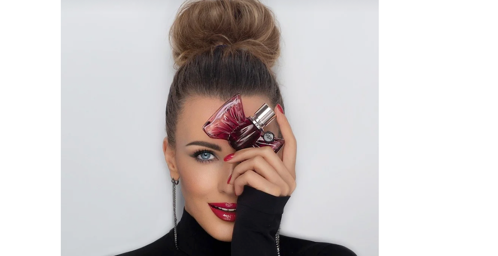 woman holding perfume bottle against her head smiling